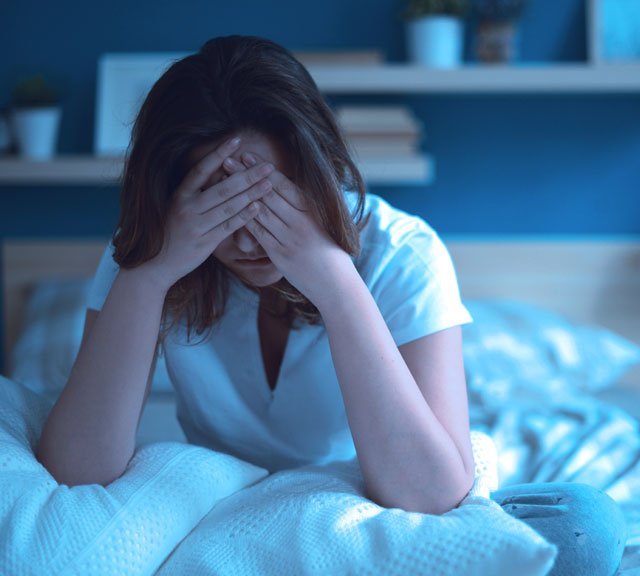Woman sitting in bed at night with stress and sleep discomfort